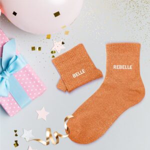 Ces chaussettes dépareillées orange à paillettes avec les mentions Belle et Rebelle en blanc.