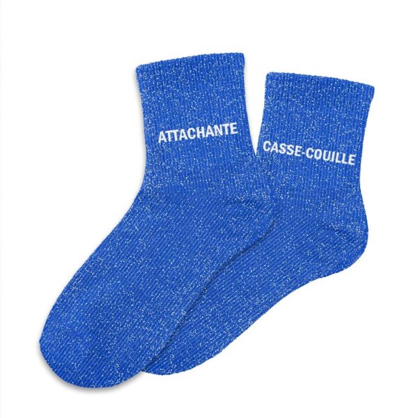Une paire de chaussettes courtes en coton, parsemées de paillettes bleues scintillantes. L'inscription "Attachante" est brodée sur une chaussette et "Casse-couille" sur l'autre, en blanc.