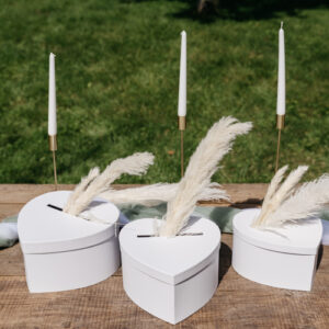 Une urne en forme de cœur blanc, posée sur une table décorée de fleurs blanches et de bougies. L'urne est mise en valeur par un éclairage doux.