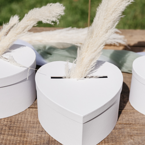 Une urne en forme de cœur blanc, posée sur une table décorée de fleurs blanches et de bougies. L'urne est mise en valeur par un éclairage doux.