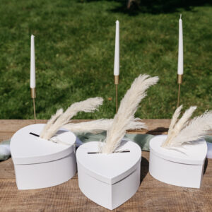 Une urne en forme de cœur blanc, posée sur une table décorée de fleurs blanches et de bougies. L'urne est mise en valeur par un éclairage doux.