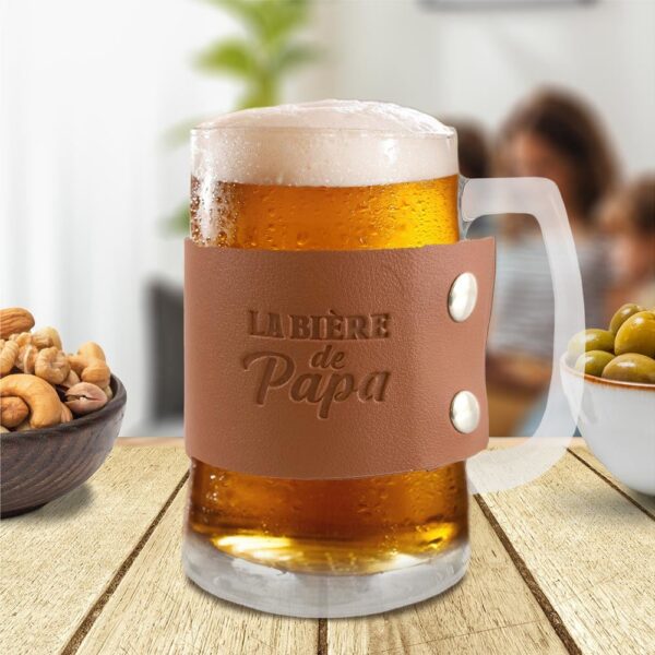 Vous cherchez un beau cadeau pour un papa amateur de bières ? Ne cherchez plus ! Notre chope de bière "La bière de Papa" est le présent idéal pour la Fête des Pères, un anniversaire, Noël, ou toute autre occasion de lui faire plaisir. Reprenant la forme classique d'une chope de bière transparente, elle est sublimée par un élégant morceau de cuir sur lequel est inscrite la mention "La bière de Papa". Un cadeau personnel et chaleureux qui fera sourire à coup sûr.