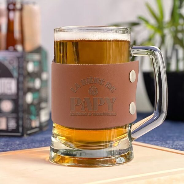 Vous cherchez un beau cadeau pour un papy amateur de bières ? Ne cherchez plus ! Notre chope de bière "La bière de Papy" est le présent idéal pour un anniversaire, Noël, la Fête des Grands-Pères, ou toute autre occasion de lui faire plaisir. Reprenant la forme classique d'une chope de bière transparente, elle est sublimée par un élégant morceau de cuir (ou simili-cuir) marron sur lequel est inscrite la mention "La bière de Papy, saveurs & traditions". Un cadeau personnel et chaleureux qui fera sourire à coup sûr.