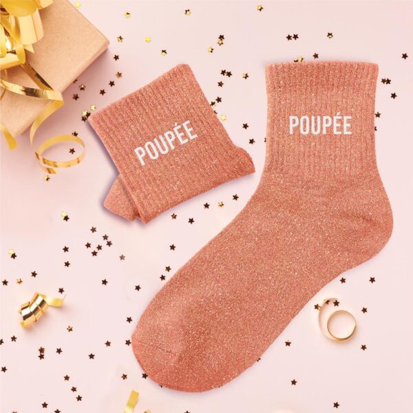 Apportez une touche de charme et de lumière à votre tenue avec nos Chaussettes Paillettes "Poupée" ! Ces chaussettes sont parfaites pour les personnalités douces et pétillantes, ou simplement pour ajouter une note de fantaisie à votre quotidien. Elles se distinguent par leur délicate couleur pêche ou corail clair, entièrement parsemée de paillettes scintillantes. Chaque chaussette est ornée de la mention "POUPÉE" en lettres blanches, pour un look à la fois stylé et affectueux.