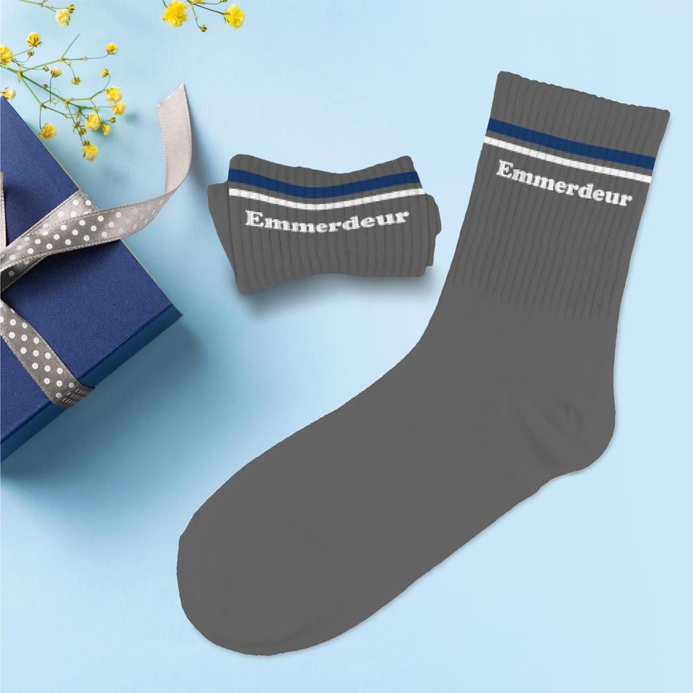 paire de chaussettes grises de coupe moyenne, avec deux fines bandes horizontales bleu marine et blanche sur le haut. Sous les bandes, le mot 'Emmerdeur' est écrit en blanc sur chaque chaussette