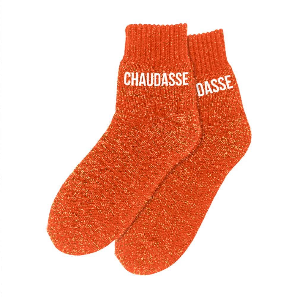 Paire de chaussettes polaires épaisses et montantes de couleur orange pailleté, avec le mot "CHAUDASSE" imprimé en blanc sur les deux pieds.