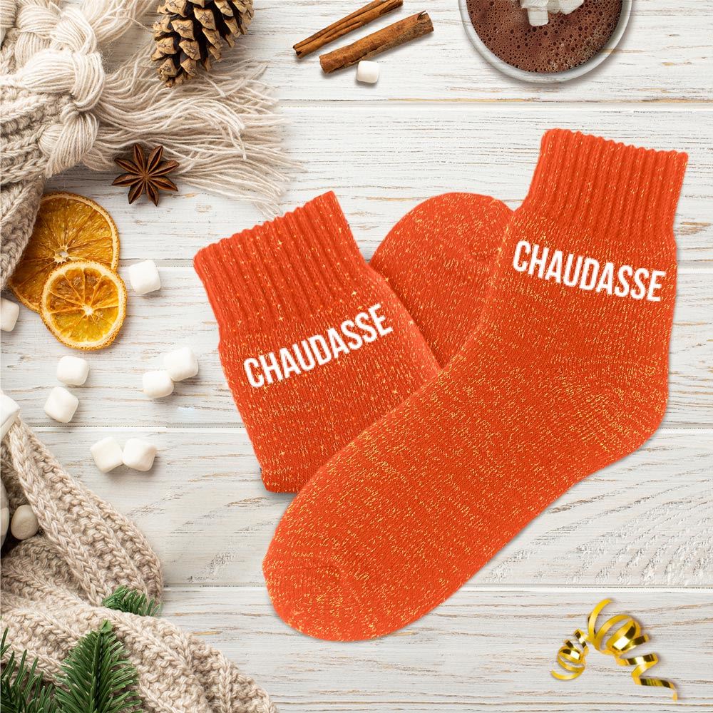 Paire de chaussettes polaires épaisses et montantes de couleur orange pailleté, avec le mot "CHAUDASSE" imprimé en blanc sur les deux pieds.