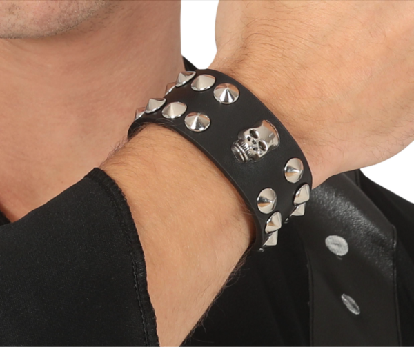 Bracelet large en cuir noir orné d'un crâne argenté central et de deux rangées de clous métalliques pointus.