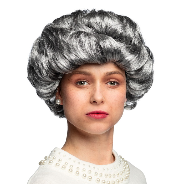 Portrait d'une femme portant une perruque grise volumineuse avec une coiffure crantée rétro, complétée par des boucles d'oreilles en perles et un haut blanc orné de perles."