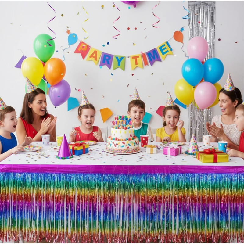 Jupe de table décorative à franges fines multicolores métallisées. Les franges présentent un dégradé de couleurs arc-en-ciel brillant (rose, jaune, vert, bleu, rouge). Le haut de la jupe possède une bordure rose fuchsia satinée.