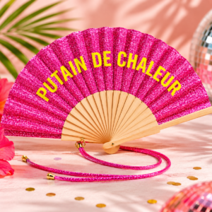 Une sélection de huit éventails colorés et pailletés ouverts, chacun doté d'une structure en bois naturel et d'un cordon de poignet scintillant assorti. Chaque éventail affiche un texte blanc ou coloré au centre : "PUTAIN DE CHALEUR" (rose), "PUTAIN J'ÉTOUFFE" (orange), "D'AMOUR ET DE PAILLETTES" (bleu), "Qué calor !" (rouge), "L'AMOUR DANS L'AIR" (rose clair), "Libre comme l'air" (violet), "La Dolce Vita" (gris argenté) et "Besoin de fraîcheur" (vert doré).